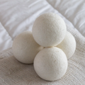 Stack of four white wool dryer balls with fuzzy felt texture on beige linen fabric.
