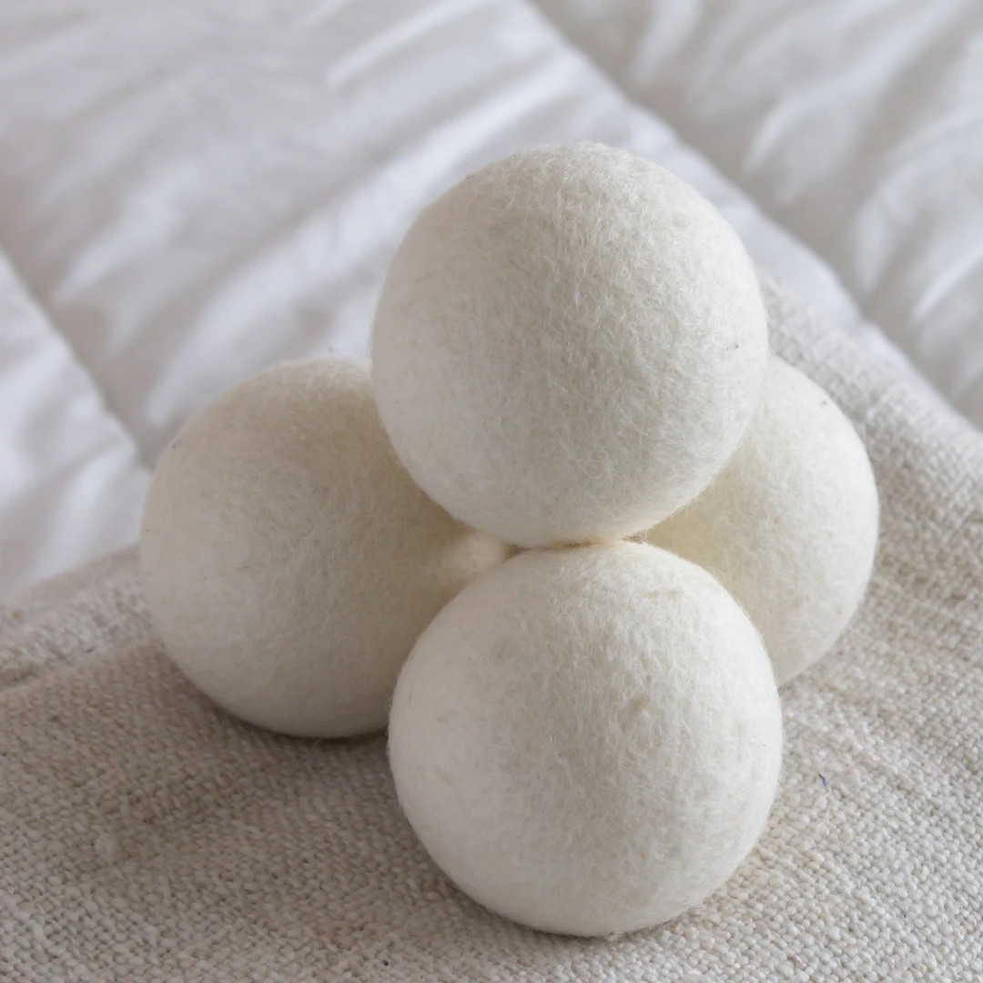 Stack of four white wool dryer balls with fuzzy felt texture on beige linen fabric.